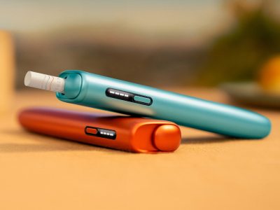 Blue IQOS ILUMA i ONE above a green IQOS ILUMA i ONE, with red background